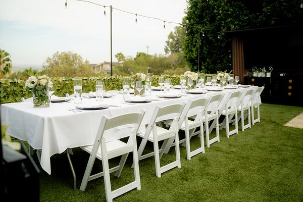 A long white table set with flowers on the lawn