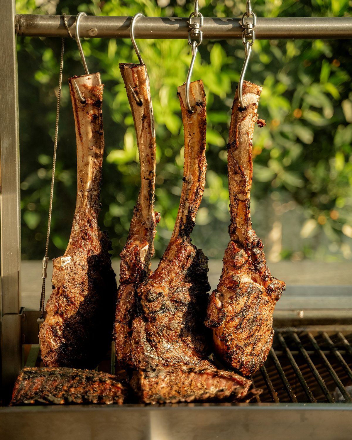 Tomahawk steaks hanging over the live fire